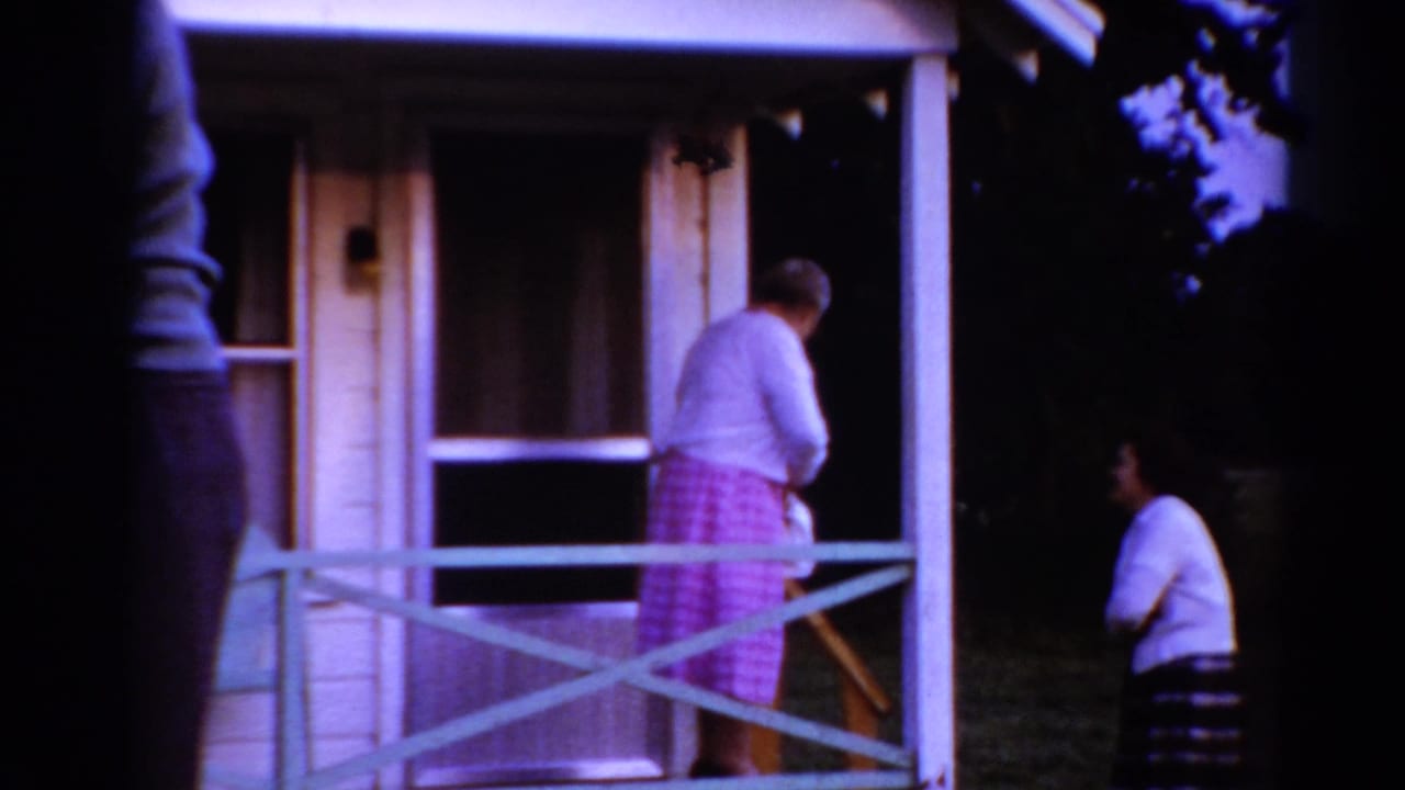 In 1964 Toledo home-movie footage, an older woman in a pink checkered dress stands on a porch as a younger woman waits below.