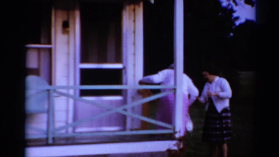 The older woman begins descending from the porch while a younger woman reaches out to assist in the Ohio home-movie scene.