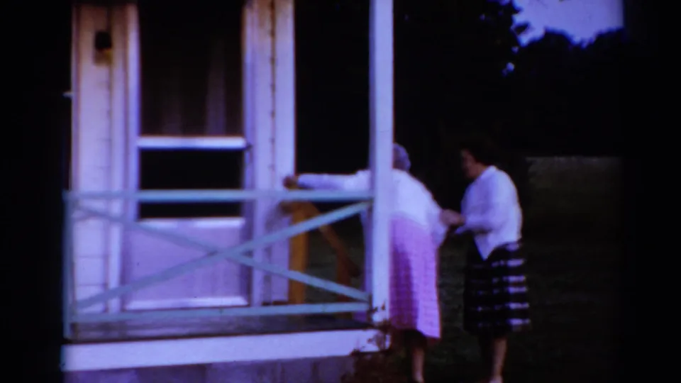 At the end of the 1964 Toledo clip, the younger woman steadies the older woman beside the porch railing and dark yard.