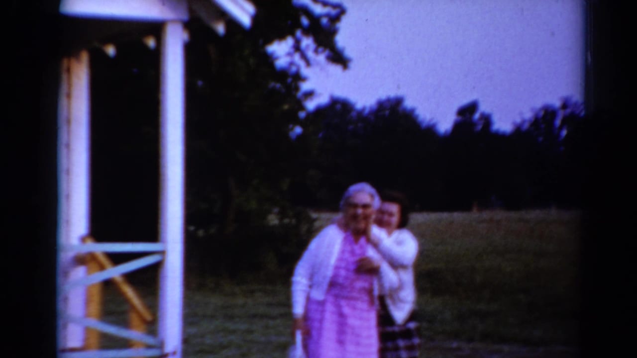 Older woman in pink walking from the house with a younger woman close behind her.