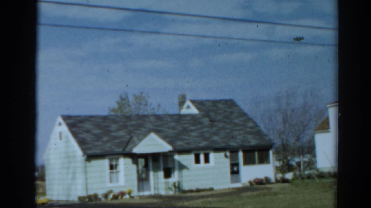 Pale one-story house with dark roof, white trim, lawn and flower beds.