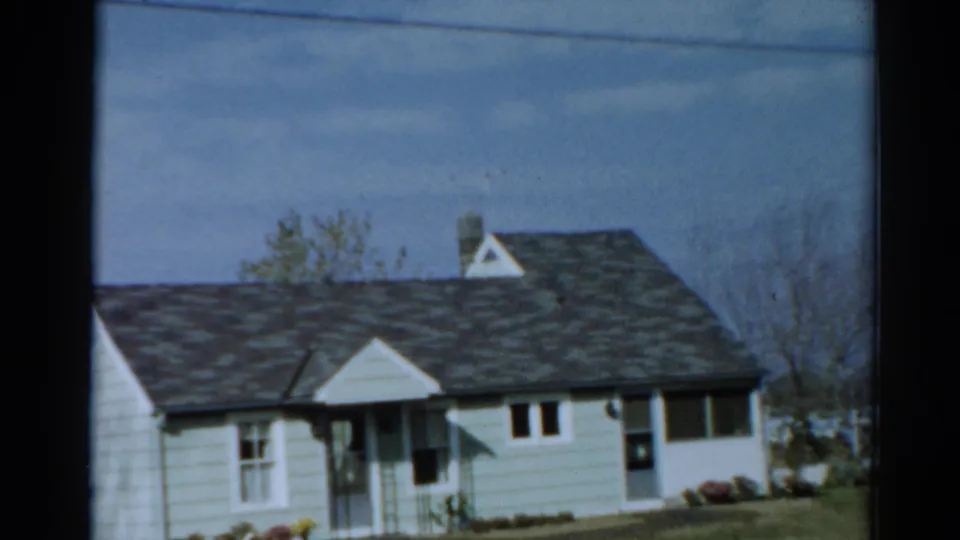 1964 Toledo exterior view of a light-colored house, showing the front porch, windows, dark roof and small landscaped yard.