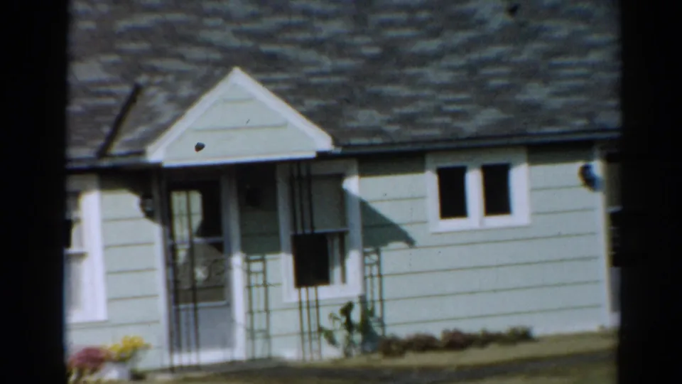 Zoomed 1964 Toledo home-movie frame showing the house porch, screen door, double windows, roof shingles and front garden.