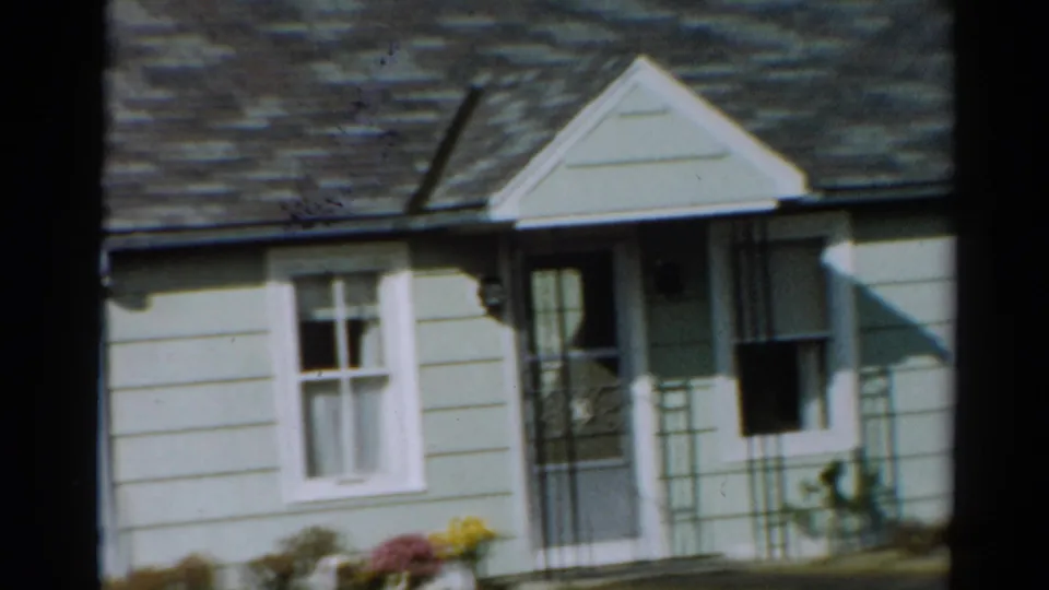 Close 1964 Toledo frame of the suburban house facade with a porch, white-trim window, screen door, siding and bright flowers.