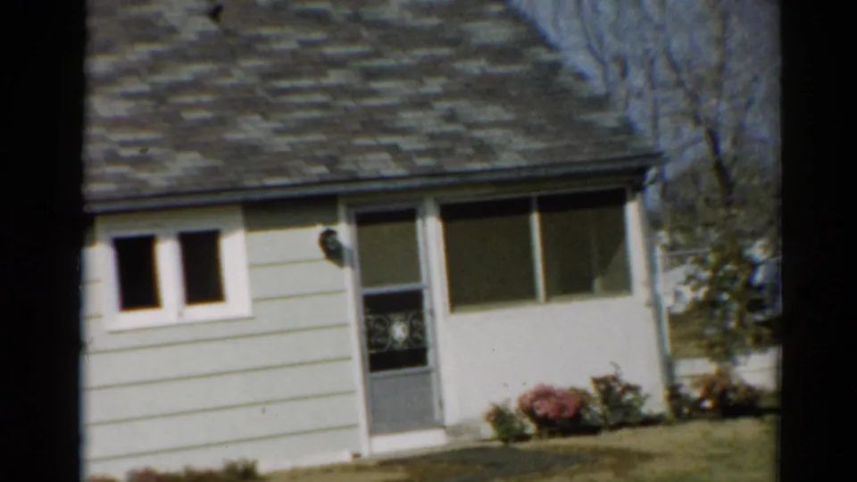 1964 Toledo exterior frame with the bungalow front centered, showing roof shingles, paired small windows, screen door, picture window, and yard plants.