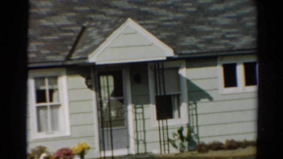 1964 Toledo home exterior with porch gable, front door area, curtained window, small side window, and flowers along the base.