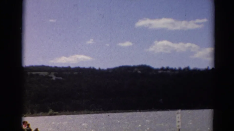 1964 Toledo-area 8mm frame showing lake water, distant wooded shoreline, low clouds, and dark gate-like borders.