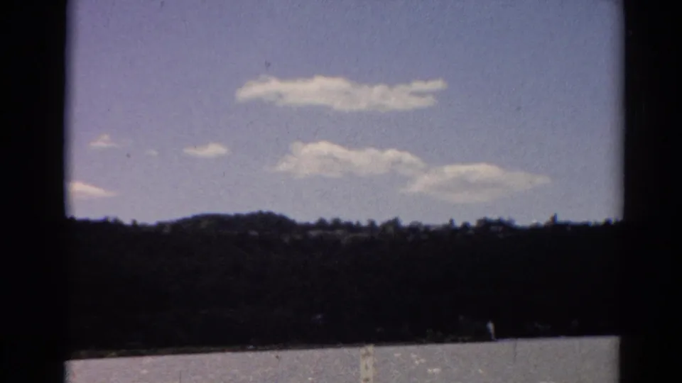 1964 Toledo-area 8mm frame with calm lake water, distant wooded shore, low hill, and scattered summer clouds.