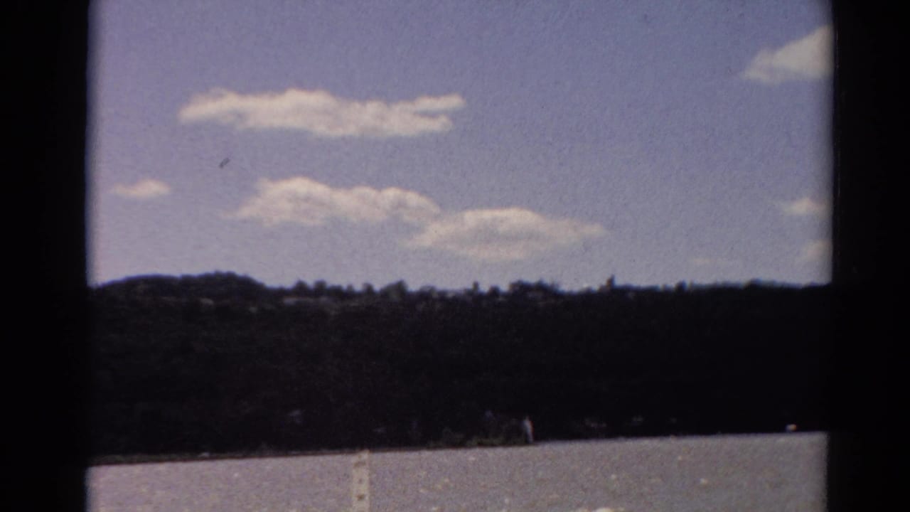 Similar lakeside view with scattered clouds and a dark tree line.
