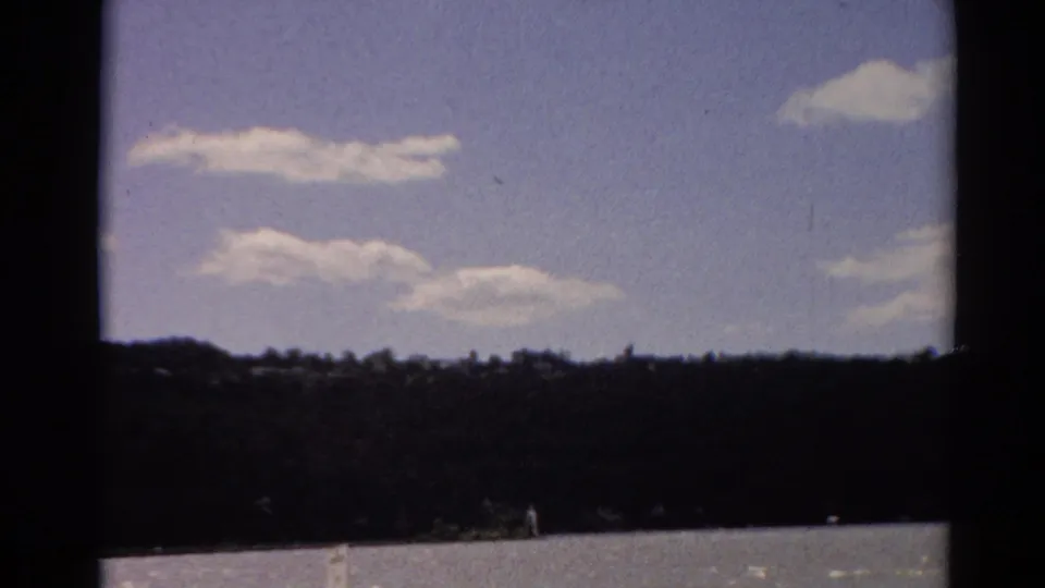 1964 Toledo home-movie view of clouds, sky, and a distant tree-lined shore.