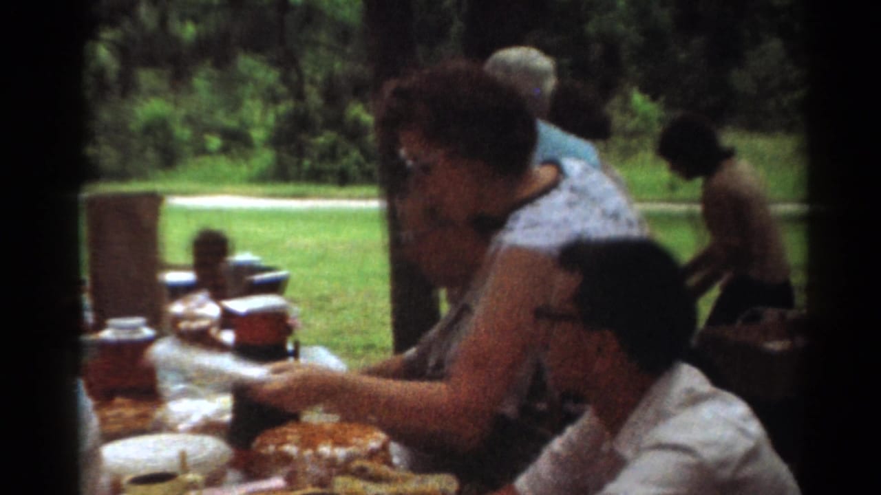 Adults sit beside picnic food and thermoses at an outdoor table.