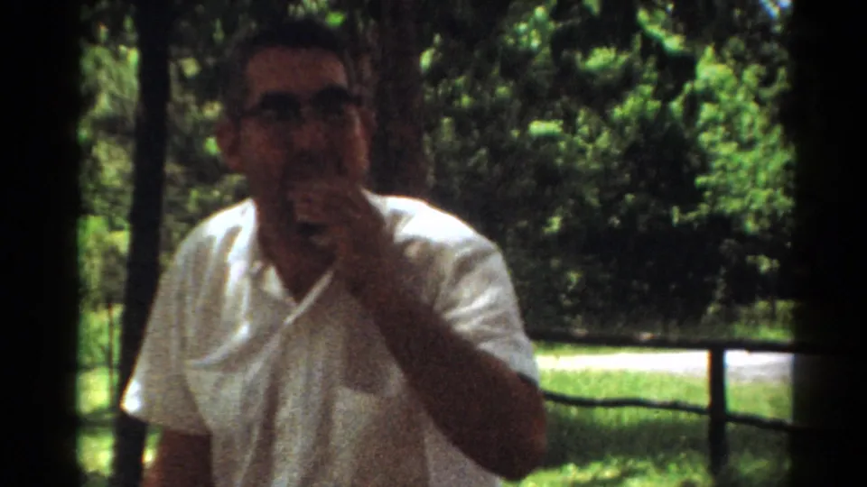 1964 Toledo park frame showing a man in a white shirt eating near a picnic area.