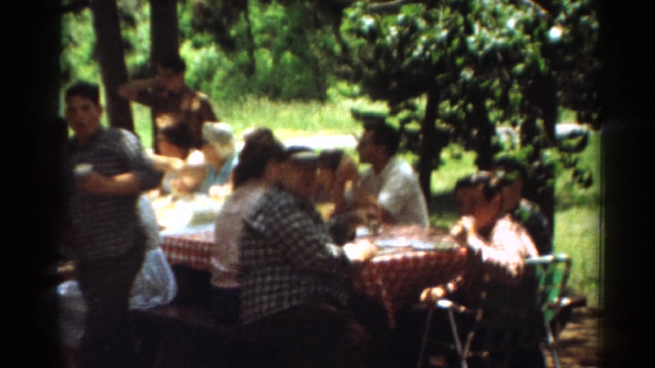 People sit at a picnic table in shade with a boy standing behind them.