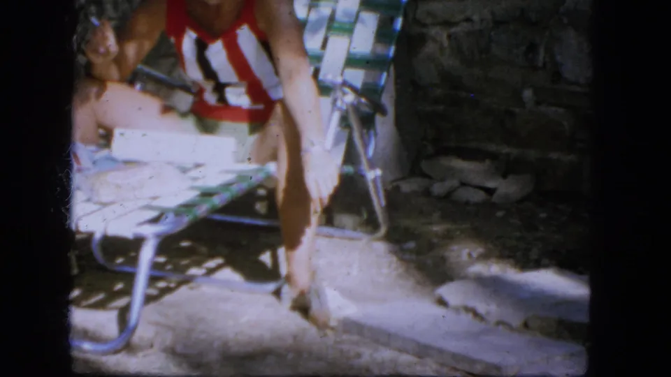 1964 Troy frame with a seated person in a striped swimsuit extending a hand toward a small chipmunk or squirrel in a backyard.