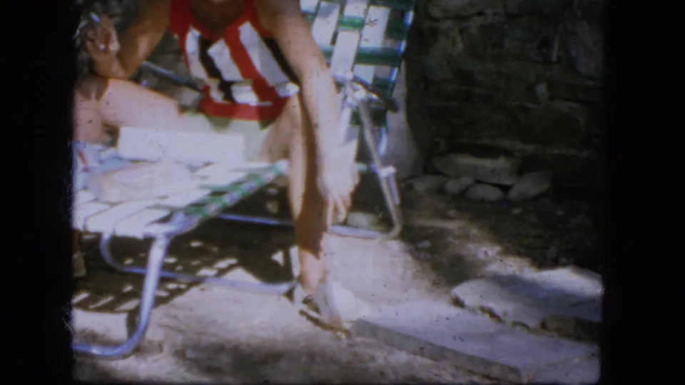 1964 Troy 8mm frame showing the seated person and striped chair as the small animal remains low near the hand and chair legs.