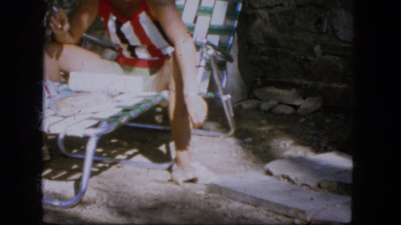 Woman in a red and white striped swimsuit lounges on a folding chair as a small rodent is near her feet.