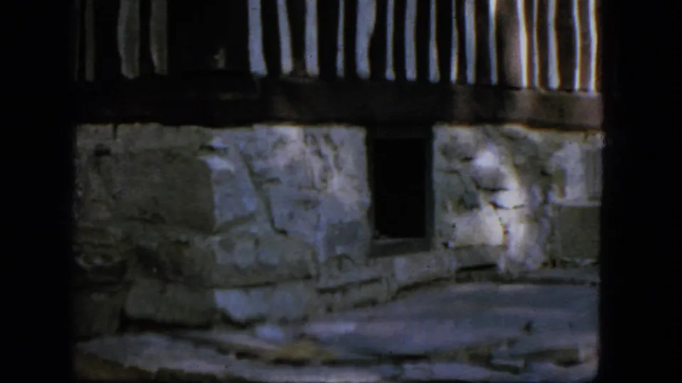 1964 Troy, New York 8mm frame showing a rustic stone exterior, railing, small window, and shaded patio area.