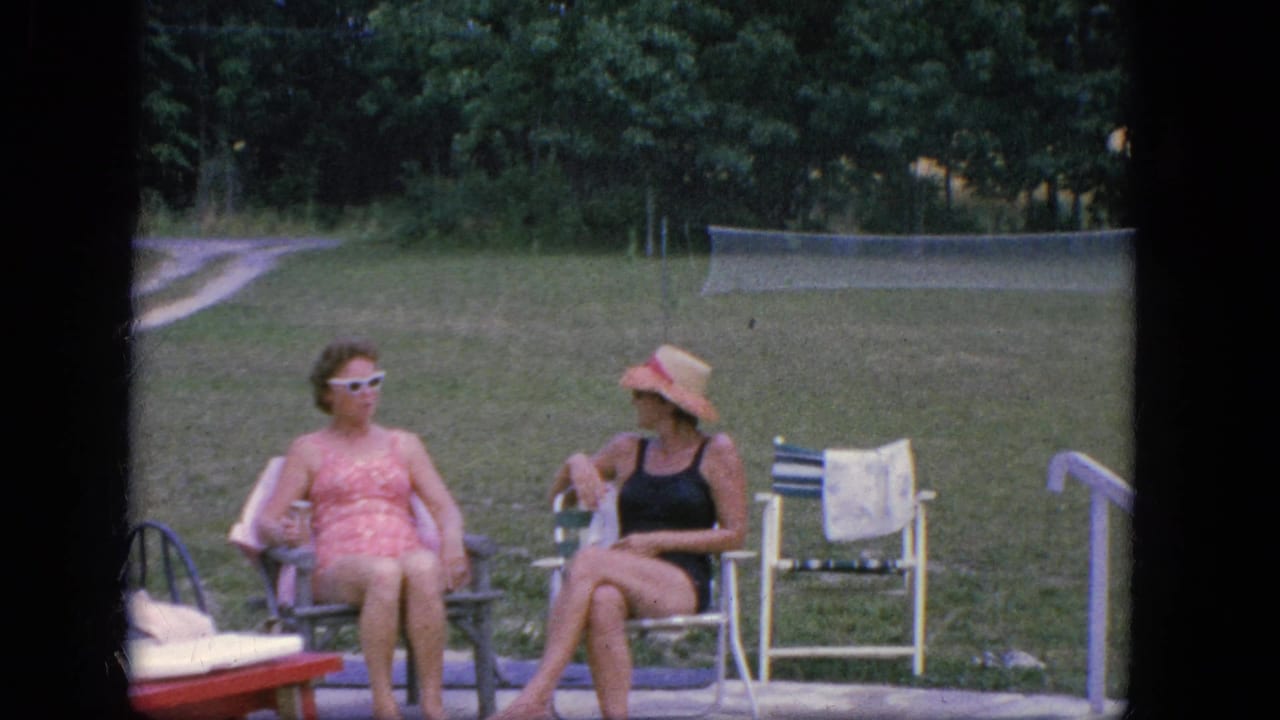 Two women sit in lawn chairs beside a pool area with grass and trees behind them.