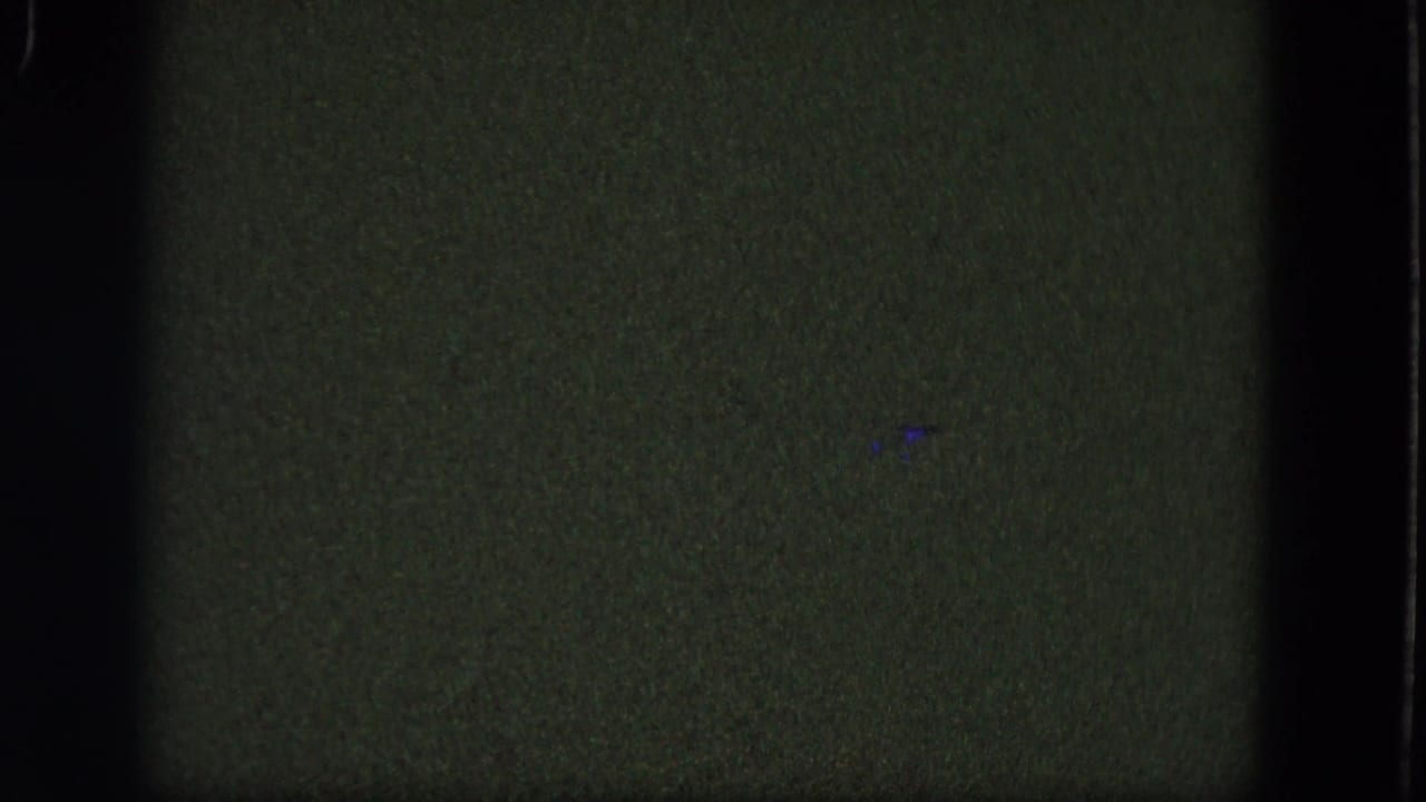 Dark greenish 8mm frame with grain, black borders, and faint blue specks.
