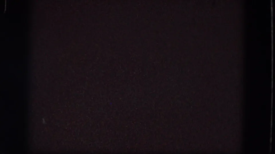 Very dark 1964 Troy 8mm frame with reddish-brown shadow, grain, gate edge, and a faint blue mark.