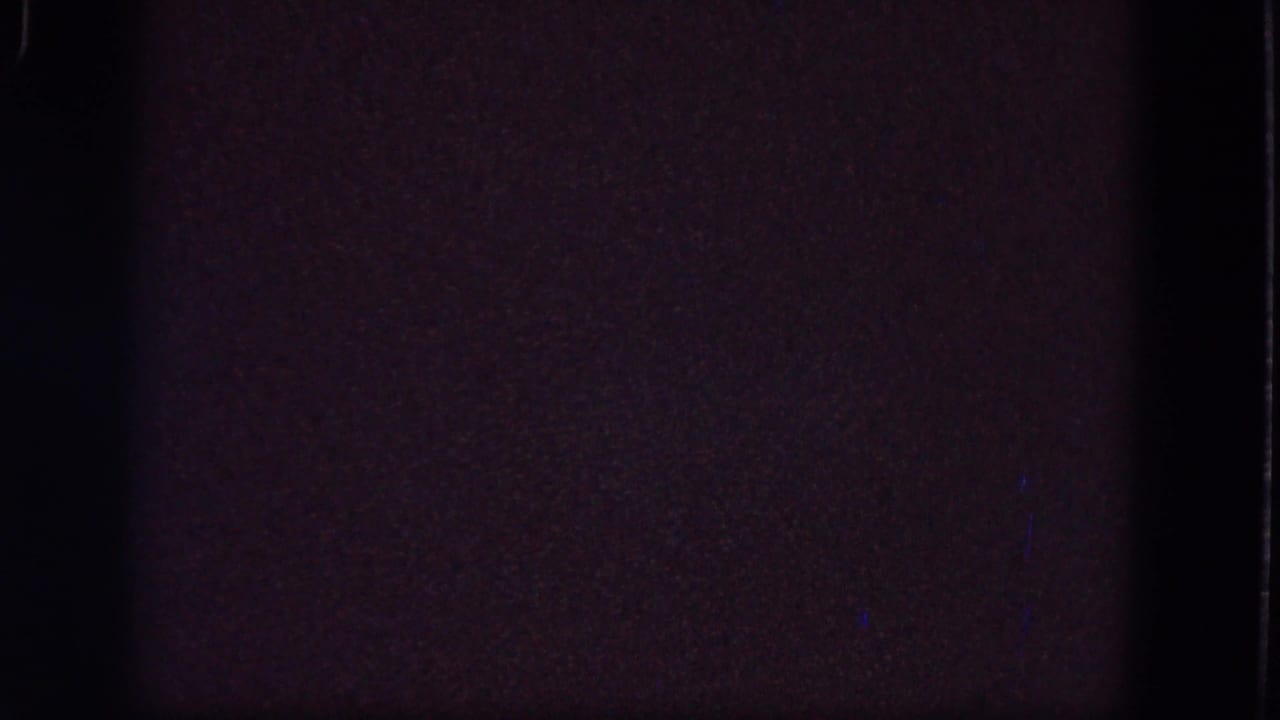 Nearly black blank frame with grain, soft edge marks, and faint color noise.