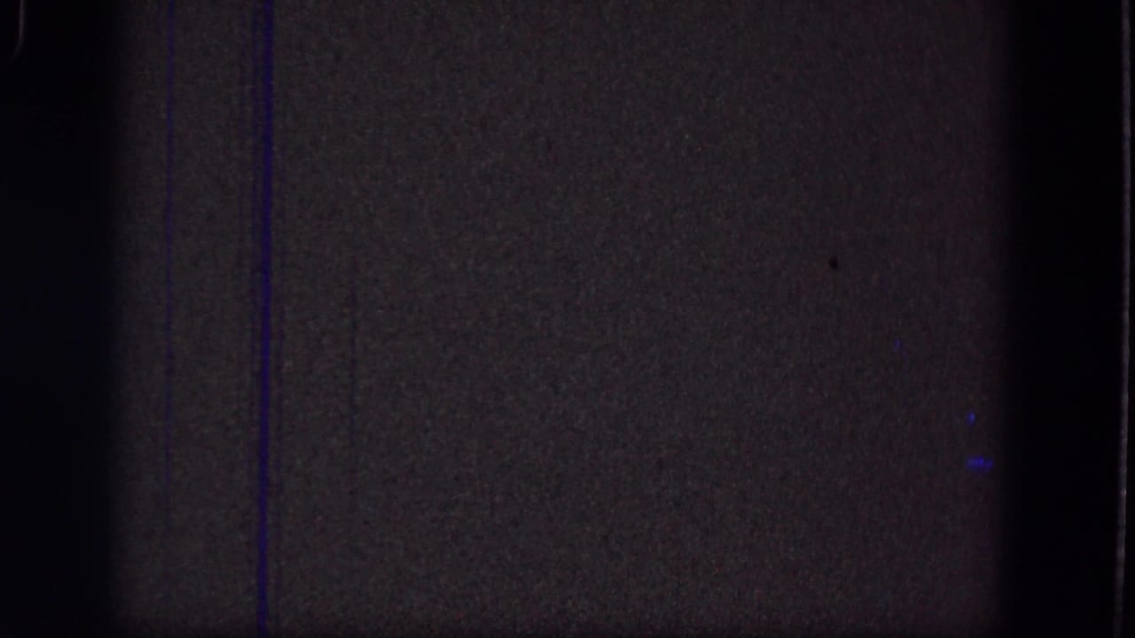 Dark grainy film frame with green-brown cast, black edges, and faint vertical blue lines.