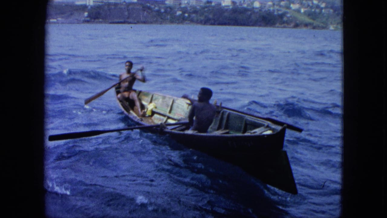A small rowboat with two men moves across rough blue water, with land beyond.