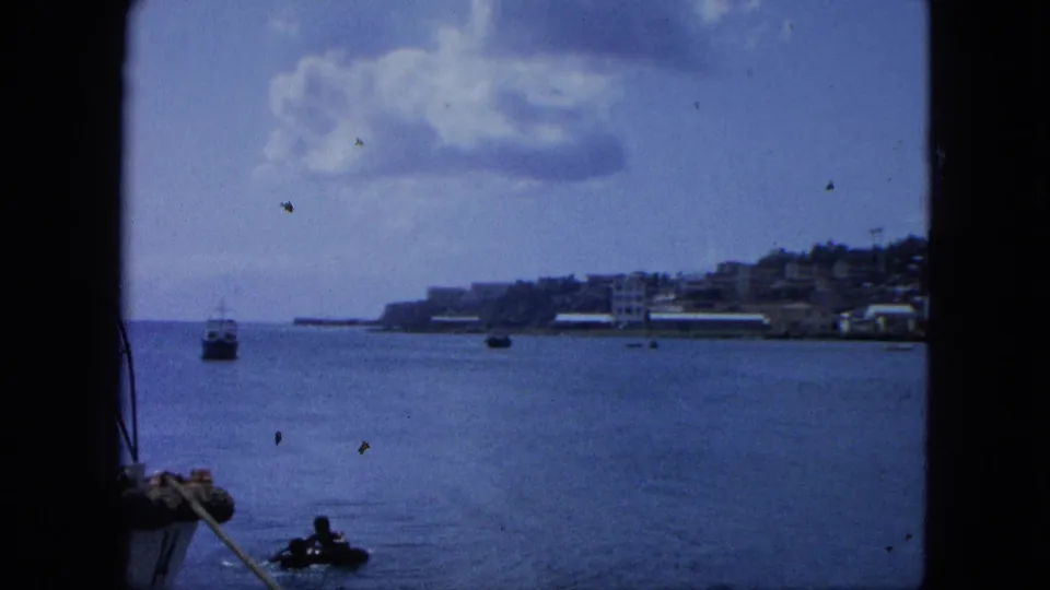 1964 United States Virgin Islands 8mm frame with open water, small boats, shoreline development, and a partly cloudy sky.