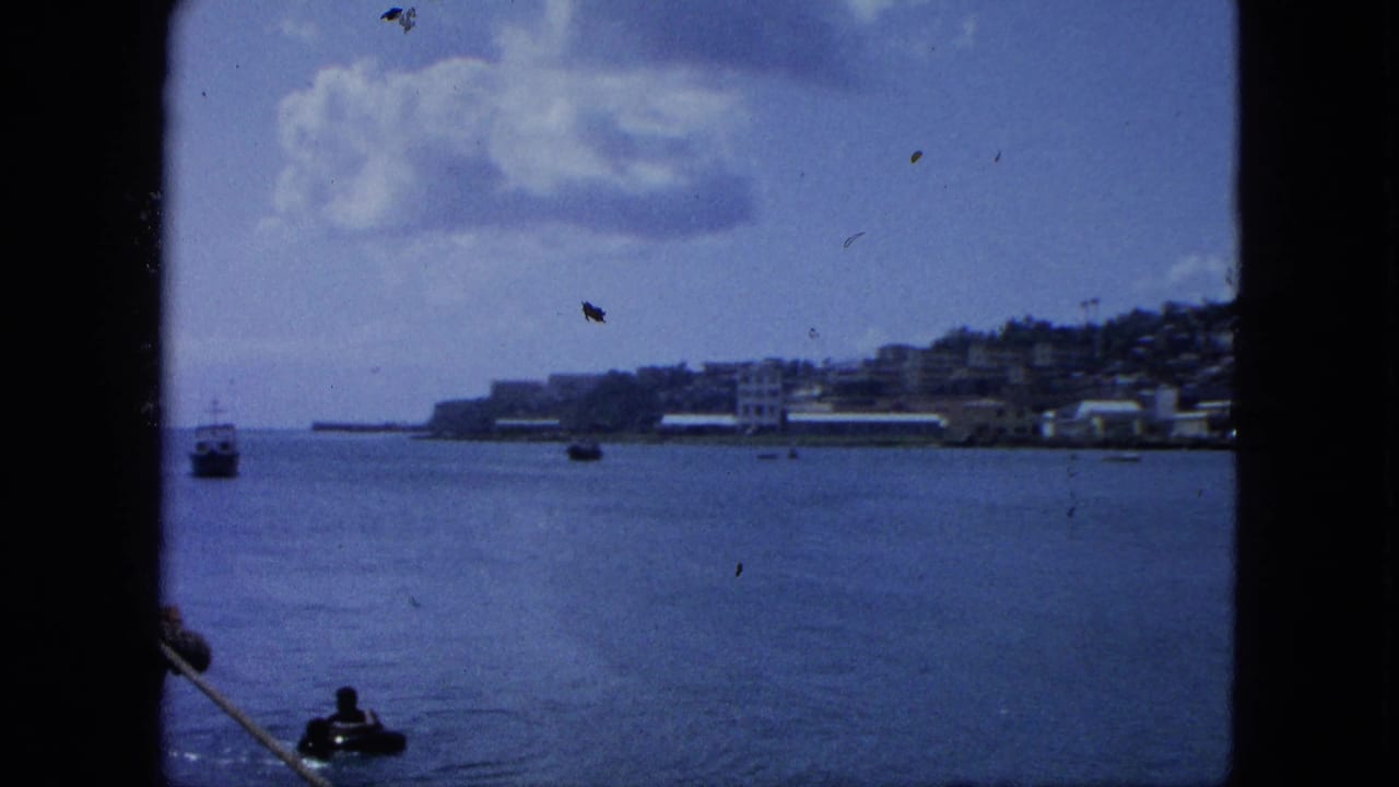 Coastal water view through a dark vessel frame, with small boats, shoreline buildings, hillside, and clouds.