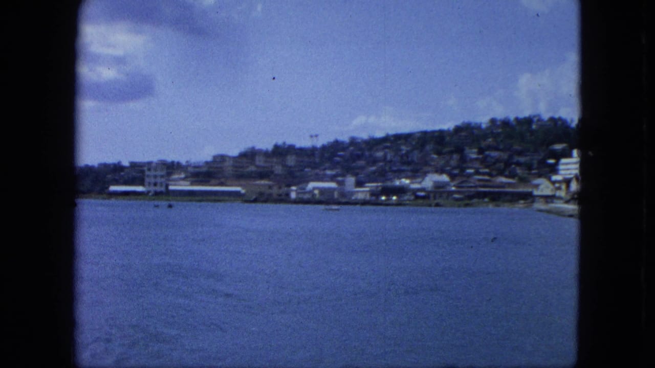Calm blue water facing a coastal town and hillside under a partly cloudy sky.