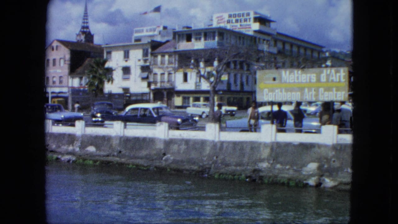 Cars pass a waterfront embankment near pedestrians and a large Caribbean Art Center sign.