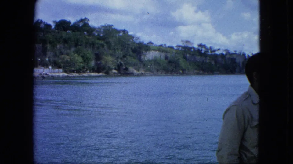 1964 8mm U.S. Virgin Islands harbor view with a partially visible adult man at the right edge near the window frame.