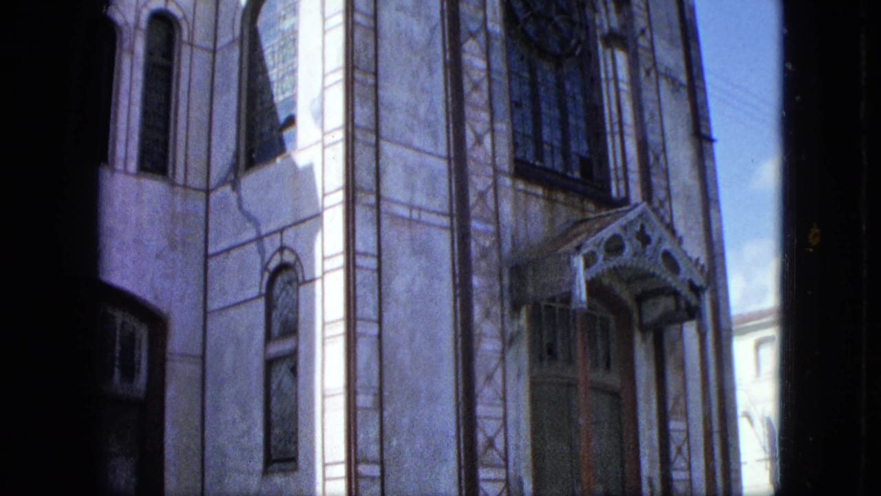 1964 U.S. Virgin Islands frame focused on the ornate building entrance with arched windows, pale masonry, and a decorative canopy.