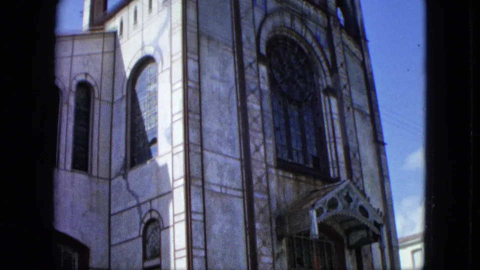1964 U.S. Virgin Islands home-movie frame showing the upper facade, large arched glazing, and ornate entrance canopy.