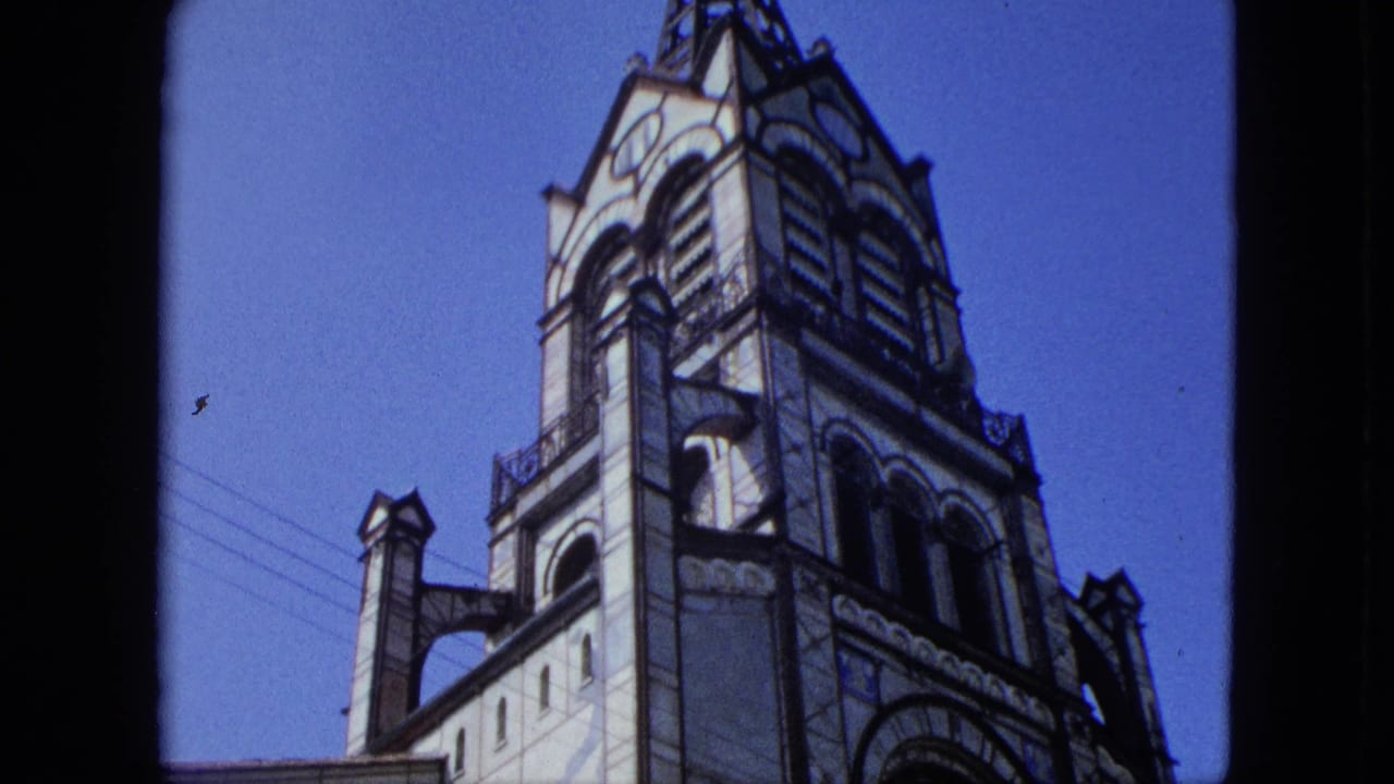 Upper portion of a church tower with decorative spire and utility wires nearby.