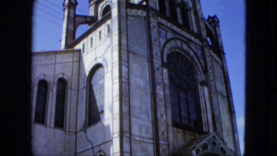 1964 U.S. Virgin Islands 8mm frame showing the church facade lower on the tower, including tall arched windows and decorative stonework.
