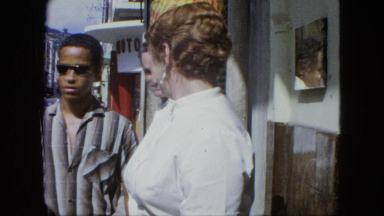 Two adults and a young man in sunglasses stand on a sunny sidewalk near a storefront.