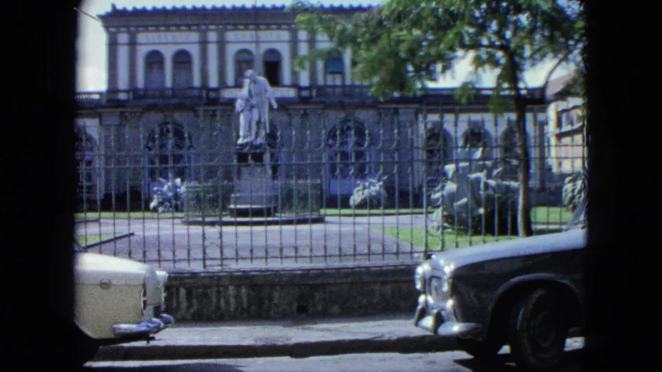 1964 USA Virgin Islands frame of a colonial-style building, standing statue, arched windows, iron fence, lawn, and partial classic cars.