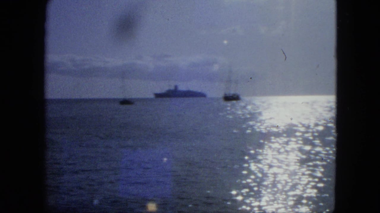 Calm ocean with two small boats and a distant large ship under bright sun glare.