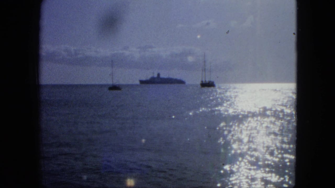 1964 USA Virgin Islands home-movie frame with a distant passenger ship, two sailboats, and sparkling glare across blue water.
