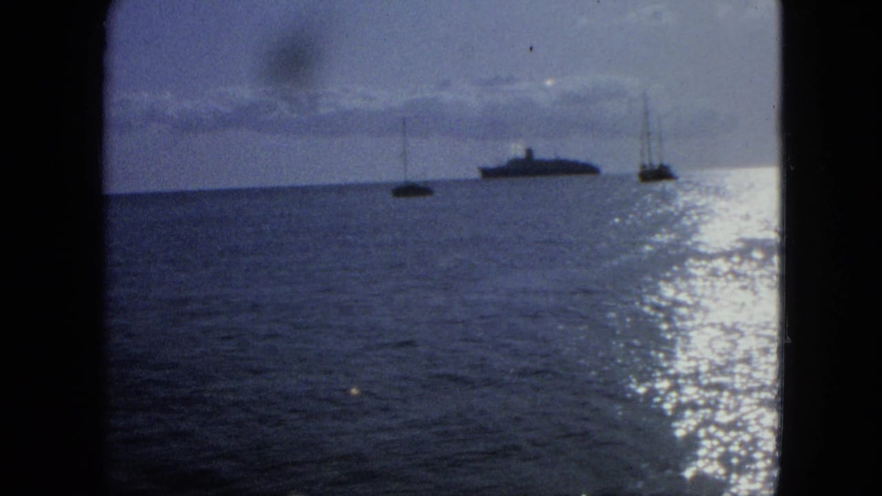 Large distant vessel between two sailboats with bright glare on the water.