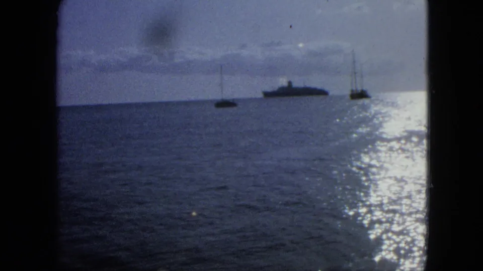 1964 U.S. Virgin Islands 8mm frame with a large offshore vessel, two sailboats, cloud band, and bright water glare.
