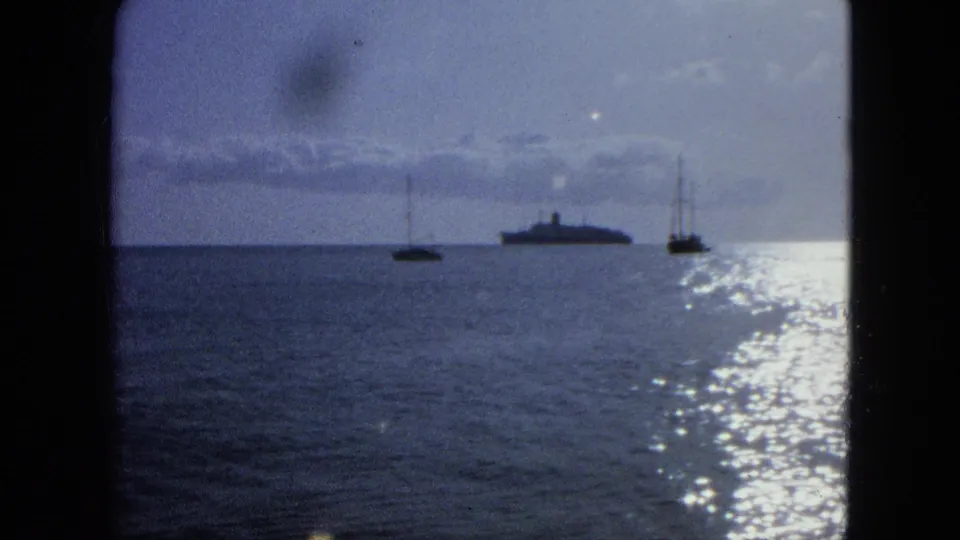 1964 U.S. Virgin Islands 8mm frame showing silhouetted offshore vessels and shimmering reflected light on the sea.