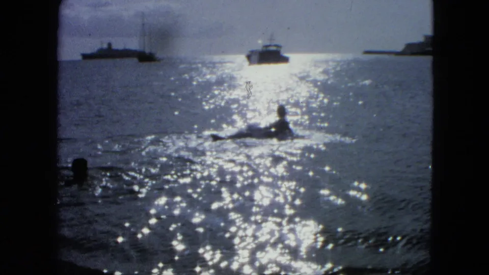 1964 8mm harbor view with sparkling water, a small figure or craft in the foreground, and distant boats near the horizon.