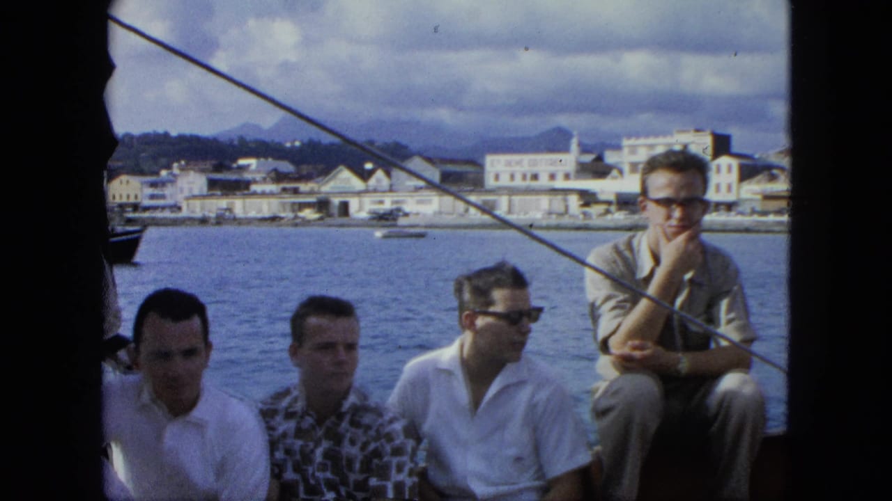 Men in casual shirts sit close together on a boat in the U.S. Virgin Islands, with harbor buildings and hills visible beyond the water.