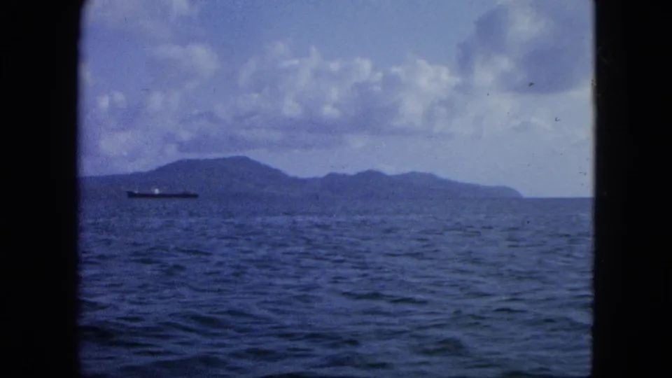 1964 8mm-style Virgin Islands ocean view with a low island on the horizon and a cargo ship at left.