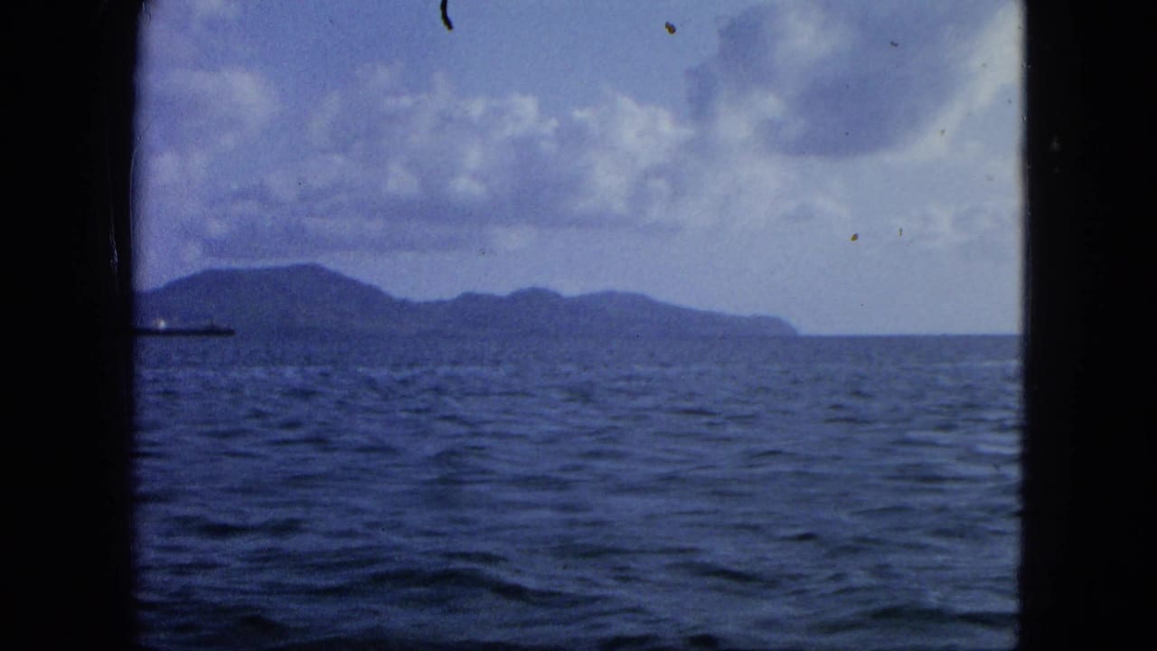 Distant island across open sea with a cargo ship partly visible near the left edge.