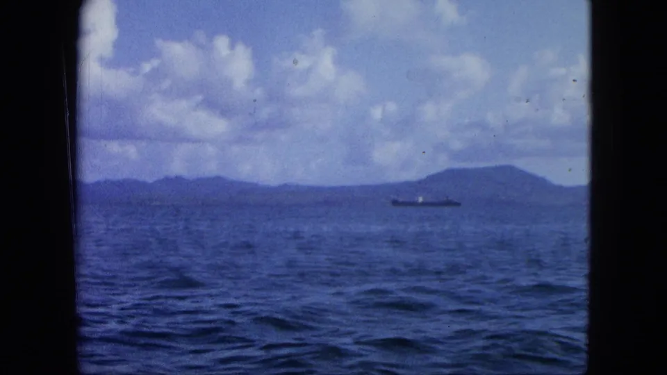 1964 Virgin Islands home-movie frame with cargo ship, distant island forms, blue sea, and soft cloudy sky.