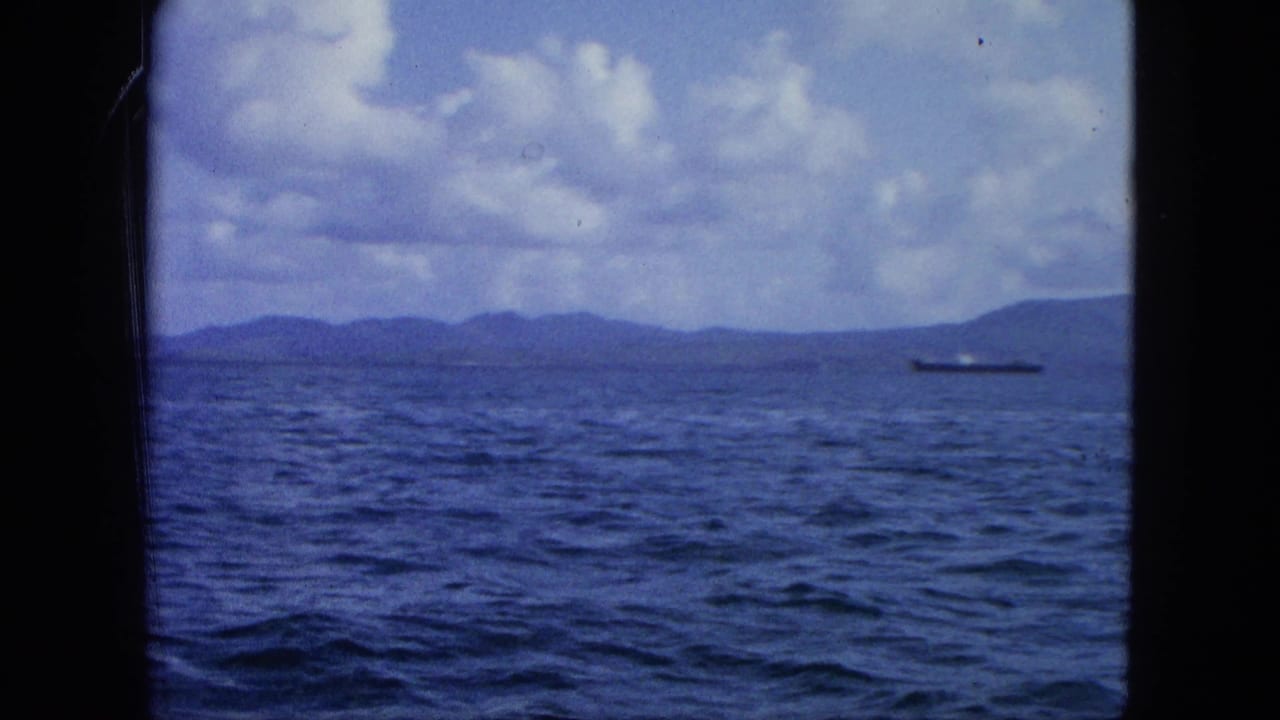 1964 8mm United States Virgin Islands footage showing open water, distant island hills, clouds, and a small vessel near the horizon.