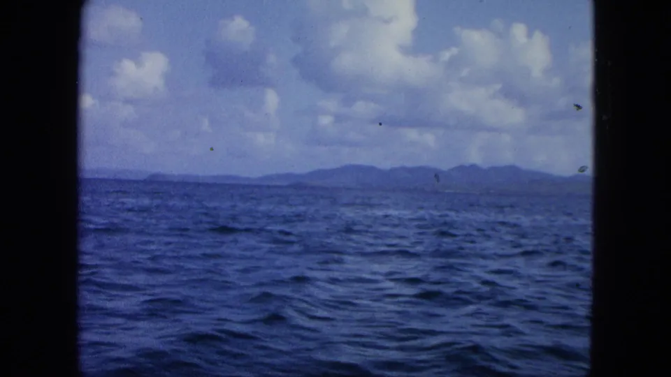 1964 8mm United States Virgin Islands footage showing a wide sea surface, distant mountainous island forms, and scattered clouds.